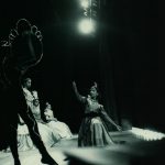 Thumbnail of One dancer kneeling with other dancers around her all wearing costumes