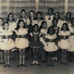 Thumbnail of Sixteen girls looking and smiling at camera wearing dresses