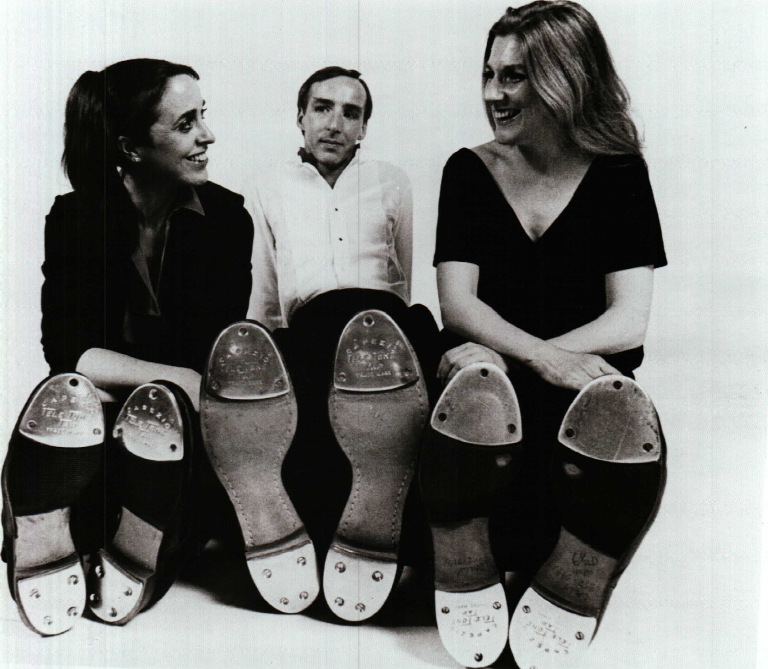 Two women and one man seated smiling with bottom of tap shoes facing camera